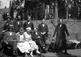 Sju män och två kvinnor sitter på, respektive står vid en bänk utanför Lungkliniken i Eksjö. I bakgrunden syns barrträd.