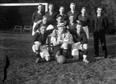 Elva män i fotbollsdräkter och en man i kostym står uppställda för fotografering vid ett fotbollsmål.