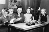 Tre flickor och en pojke stående vid katedern, fröken sittande. Adventsljusstake på katedern. Gamla Sinntorpskolan.