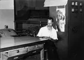 Maskinförare Kurt Floman läser vid förarbordet PM 10 på Papyrus i Mölndal år 1962. Till höger manöverskåpet. Affisch med kvinna på väggen.