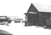 En ladugård vid Ranntorp 1:3 i Lindome. Utanför ladan står en bil och en lastbil med kran. Bilden är tagen under 1990-talet.