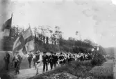Festtåg med flaggor och musikkår vid Råda kyrka i samband med en sommarfest. I spetsen går ingenjör Falgren. Okänt årtal.