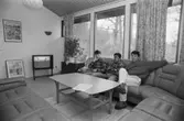 Ett allrum där tre män sitter i en soffa. Dokumentation av Sagåsens flyktingförläggning, 1992.