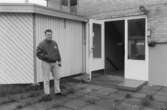 Dokumentation av Sagåsens flyktingförläggning 1992. En man står utomhus, framför ett insynsskydd, bredvid en entrédörr.