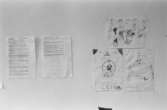 Dokumentation av Sagåsens flyktingförläggning 1992. En vägg där det till vänster sitter två maskinskrivna blad, och till höger sitter tre barnteckningar uppsatta.