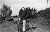 Elis Andersson och dottern Hjördis står vid en cykel på Varvsvägen i Lindome 1950. Elis Andersson var brandchef vid Lindomes borgarbrandkår.