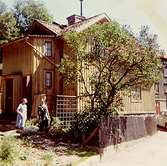 Bostadshuset Roten F25, Trädgården, år 1968. Ena gaveln med ett träd och några personer vid sidan av.