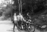 Bror Eriksson samt Helmer och Astrid Garthman som står på en landsväg brevid sin motorcykel Husqvarna 175cc (kallades Drömbåge). Mölndal, 1960-tal.