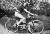 En ung kvinna som sitter på en damcykel, 1930-tal. Kamrat till fotografen Astrid Garthman. Skänkt av sonen Alf Garthman som arbetade under många år på Mölndals stadsmuseum.