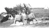 Helmer Garthmans kompisar, från vänster: Anna Nilsson, Wilgot och Gitt Ullberg
. De sitter på en filt framför en buske vid sjön Lygnern i Fjärås. Okänd man i bakgrunden. 1930-tal.