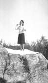 Astrid Garthman, snyggt klädd i hatt, kofta och kjol, står på en klippa och siktar mot fotografen för att kasta en snöboll. Mölndal, 1940-tal.