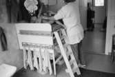 En kvinnlig förskollärare byter blöjor och kläder på ett naket barn som ligger på ett skötbord. En liten stege finns upp till skötbordet. Vid sidan av hänger handdukar på rad.