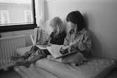 Stina och Cecilia sitter på några madrasser bredvid ett fönster, och bläddrar i var sin bok. Lunkentussen, Katrinebergs daghem.