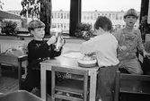 Tre pojkar sitter vid ett barnbord och leker med Duplo-lego. Vid sidan av dem står en docksäng. I bakgrunden syns fönster med Åbyskolans fasad. Katrinebergs daghem, 1992.