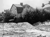 Barnhemsgatan 16 (f.d Ahlbergs skrädderi) bakifrån och delvis skymt av grönska. Man ser en mängd grushögar upplagda vid bygget av Mölndalsbro 1975.