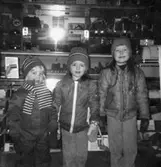 Tre höst-/vinterklädda barn som står i en affär. De kommer från Holtermanska daghemmet, 1973.