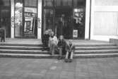 Fyra ungdomar sitter på en trappa på Brogatan. Mölndalsbro i dag - ett skolpedagogiskt dokumentationsprojekt på Mölndals museum under oktober 1996. 1996_1052-1060 är gjorda av högstadieelever från Kvarnbyskolan 9C, grupp 2. Se även 1996_0913-0940, gruppbilder på klasserna 1996_1382-1405 samt bilder från den färdiga utställningen 1996_1358-1381.