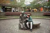 En kille sitter vid en skulptur på Alberts torg. Mölndalsbro i dag - ett skolpedagogiskt dokumentationsprojekt på Mölndals museum under oktober 1996. 1996_1227-1245 är gjorda av högstadieelever från Kvarnbyskolan 9D, grupp 6. Se även 1996_0913-0940.