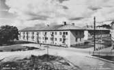 Man ser Rygatan 13-15. I bakgrunden ses Brunnsgatan 4 och längst till höger skymtar Rygatan 17. De två förstnämnda husen uppfördes 1949. Vykortet har producerats av A-B Jolin & Wilkenson, Göteborg. Kortet är märkt 