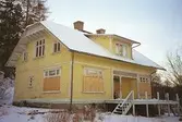 Villa Solbacken i Krokslätt, januari 1995. Ett 2-plans bostadshus med gul träpanel där vissa fönster är igenbommade. Vit altan där staketet är borttaget.
