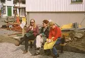 Tre kvinnor sitter på en parksoffa vid Lyktplatsen, Kvarnbydagen 25/4 1993. Gatlyktan (ej i bild) invigs. Kråkans Krog (vitt hus med grön dörr) ses till vänster.