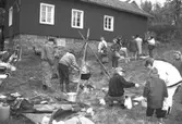 Familjesöndag vid Börjesgården, 1994-05-15. Besökare ser på när Museichef Mari-Louise Olsson kokar soppa över öppen eld. Sittandes på huk är museitekniker Alf Garthman.