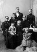 Familjeporträtt taget runt sekelskiftet i ateljé, föreställande man, hustru, fem barn samt troligtvis mor/farmoder.