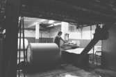 En man i arbete med en pappersbal, 1980-tal.
Bilden ingår i serie från produktion och interiör på pappersindustrin Papyrus.