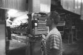 Mannen på maskinen är Juris Kuvalds och mannen i förgrunden är Lars Neckén, KM 2 i Byggnad 6, 1980-tal.
Bilden ingår i serie från produktion och interiör på pappersindustrin Papyrus.