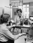 Från rundvandringen på postkontoret Stockholm 12. Fru Birgit
Hongslo, kurator vid Lidingö läroverk, agerar kund vid kassa 8 och
tittar på kassaregis-terapparaten, som används för inbetalningskort,
postanvisningar, postförskott och postsparbank.