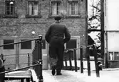 Herr Larsson på väg över Forsebron i Mölndals Kvarnby en vinterdag ca 1966-1967. I bakgrunden ses byggnaden Kvarnbygatan 41, tidigare brandstation och garage för polisbilar, numera Mölndals målarskola.