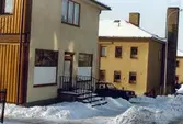 Hus på Brunnsgatan i Ryet, Mölndal, en vinterdag på 1970-talet. Huset närmast inrymmer Dahlbjörks affär.