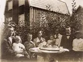 Vuxna och barn sitter kring ett kaffebord i vad som ser ut att vara en berså i trädgården. I bakgrunden syns ett hus.
Från vänster Frans Arvid Lindkvist f. 1890, Rosa Lindkvist f. 1919, Erik Lindkvist f. 1912, Anna Teresia Lindkvist f. 1895, Elna Börjesson f. 1916, Hilda Börjesson Hallgren f. 1883, Gustaf Adolf Hallgren f. 1899 och Åke Börjesson f. 1910. 
Familjen Lindkvist hyrde övervåningen av Alfred Persson.