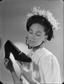 Kvinna med blomsterprydd huvudbonad håller upp en sko