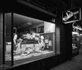 Broddmans foto
Exteriör, upplyst skyltfönster kvällstid, butiken Skivan