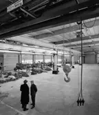 Portar
Interiör, reservdelslager. Två samtalande herrar i förgrunden, snett uppifrån.