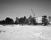 Bostadsområde
Exteriör, nästan färdiga flerbostadshus i fonden med tallar och lyftkran. Snötäckt fält i förgrunden.