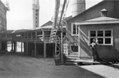 Lagerbyggnad 110 och 111 under uppbyggnad på Papyrus fabriksområde, 25/7-1945. En man är med på bilden. Transportgång och kiosken. Bakom kiosken Nedre ångcentralen.