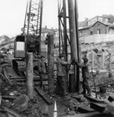 Byggnad N:o 6, tillbyggnad 1954. Pålning.
Tre okända män.