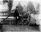 En man med cykel vid grinden.
Bostadshus i bakgrunden.