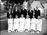 Tio konfirmander, sex flickor, fyra pojkar och pastor Hedberg.
Almby kyrka i bakgrunden.