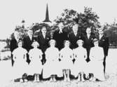 Tolv konfirmander, sex flickor, sex pojkar och pastor Ljunggren.
Hovsta kyrka i bakgrunden.
Pingstafton den 27 maj 1950.