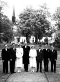 Sju konfirmander, två flickor, fem pojkar och pastor Hedström.
Kils kyrka och kyrkogård i bakgrunden.
Pingstafton den 27 maj 1950.