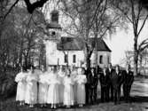 Konfirmander, 8 flickor, 5 pojkar och prosten Areborg.
Ödeby kyrka i bakgrunden.