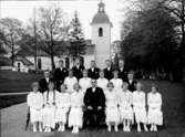 Konfirmander, 12 flickor, 7 pojkar och prosten Areborg.
Lillkyrka kyrka i bakgrunden.