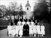 Konfirmander, 12 flickor, 7 pojkar och prosten Areborg.
Lillkyrka kyrka i bakgrunden.