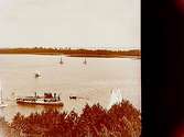 Ångslupen Hemfjärden vid Hjälmarbadens brygga, fem segelbåtar och en roddbåt. Ässön i bakgrunden.
Stereofotografi.