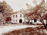 Bondsätters gård, tvåvånings bostadshus med frontespis. 15 personer framför byggnaden.
Erik Larsson
(Redaktör Saxon).