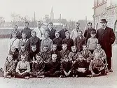 Norra Folkskolan, 31 skolpojkar med lärare, sal 18. Skolbyggnad i bakgrunden.
Ordningslärare K.E. Linderholm