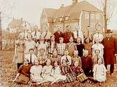 Almby Folkskolan, en och en halvvånings skolbyggnad i bakgrunden.31 skolbarn med lärare Gustaf Karlsson.